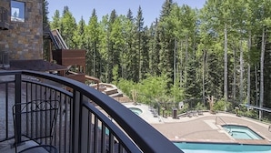 A pool area with a stone building, a deck, and a forested backdrop. - Bear Creek Lodge 208 2 Bedroom Condo by Alpine Lodging Telluride (Telluride)