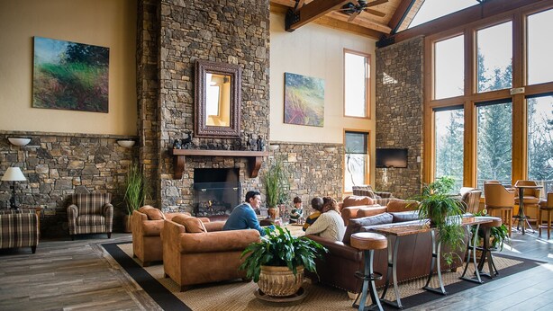 Un salón amplio con chimenea de piedra, asientos cómodos y ventanas grandes con vistas al exterior.