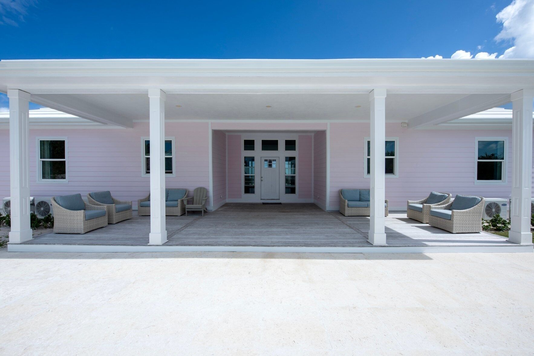 A covered porch with wicker furniture and a pink building in the background.