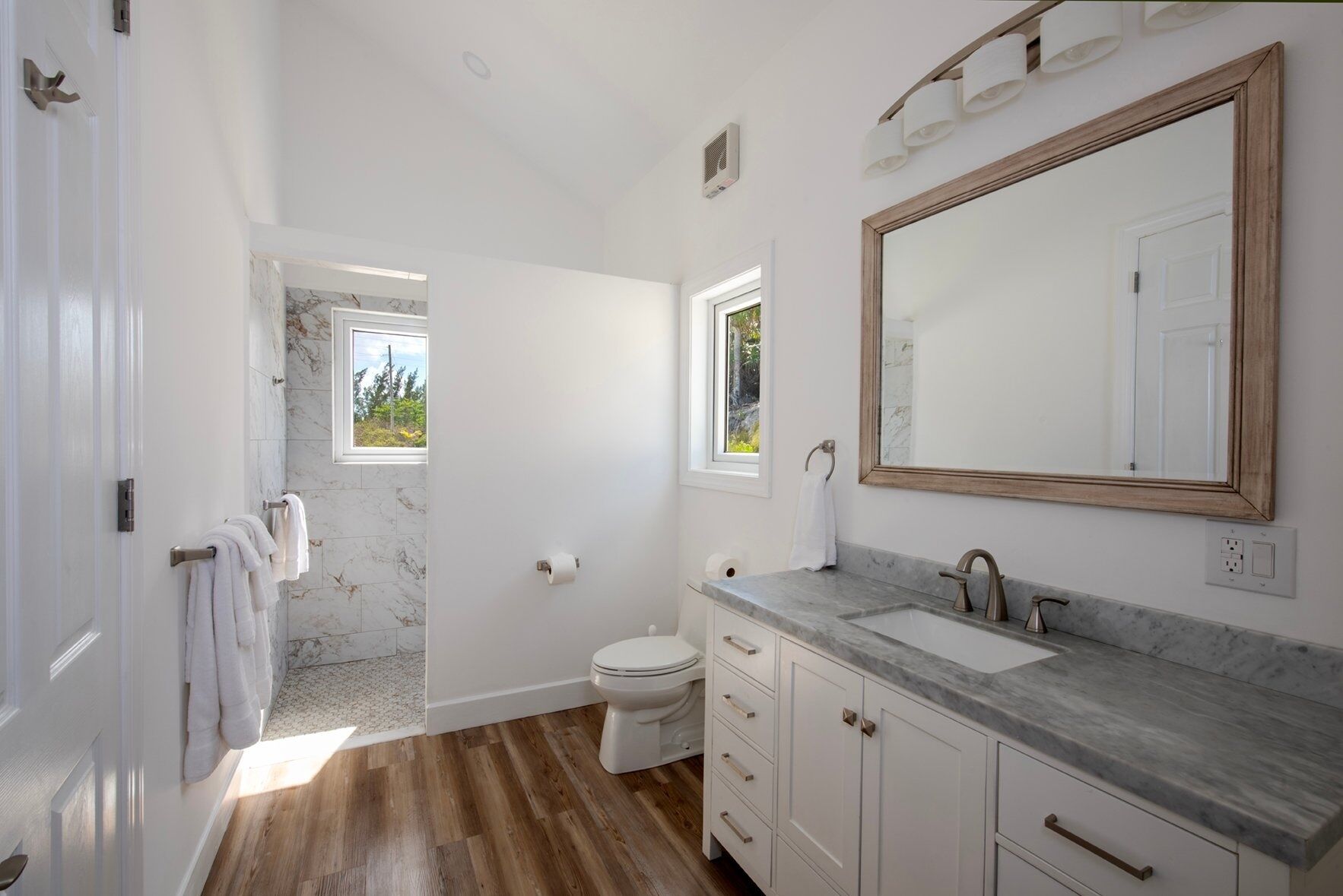 Une salle de bain moderne avec un lavabo en marbre, un grand miroir et un espace douche donnant sur un paysage verdoyant.