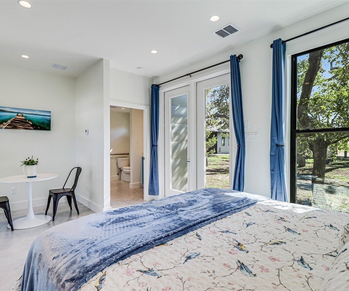 Un dormitorio con cama, escritorio y silla. Hay una ventana con cortinas y vistas al exterior.