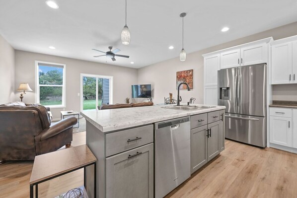 A modern kitchen with a central island, stainless steel appliances, and a dining area with a sofa and table. - Home away from Home, upscale townhome (Plover)