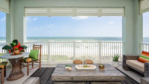 A balcony with a view of the ocean, furnished with a table, chairs, and a sofa. - Luxury 5th floor oceanfront condo 754 at Cinnamon Beach! (Palm Coast)