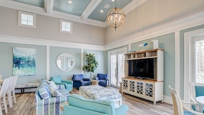 A spacious living room with a large TV, comfortable seating, and a ceiling fan. - Luxury 5th floor oceanfront condo 754 at Cinnamon Beach! (Palm Coast)