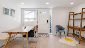 A modern, well-lit room with a wooden dining table, chairs, a blue cushioned chair, a wooden bookshelf, and a door with a frosted glass panel.