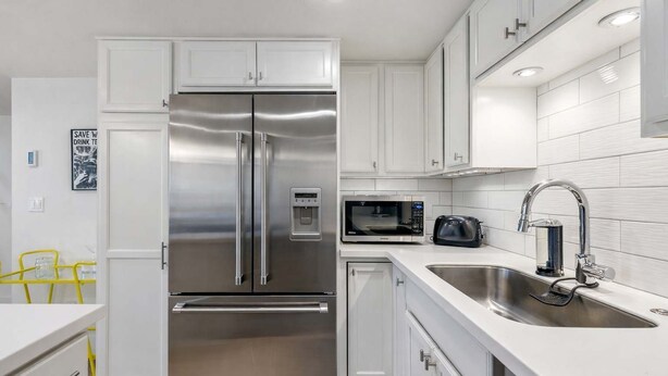 A modern kitchen with white cabinetry, stainless steel appliances, and a built-in sink.