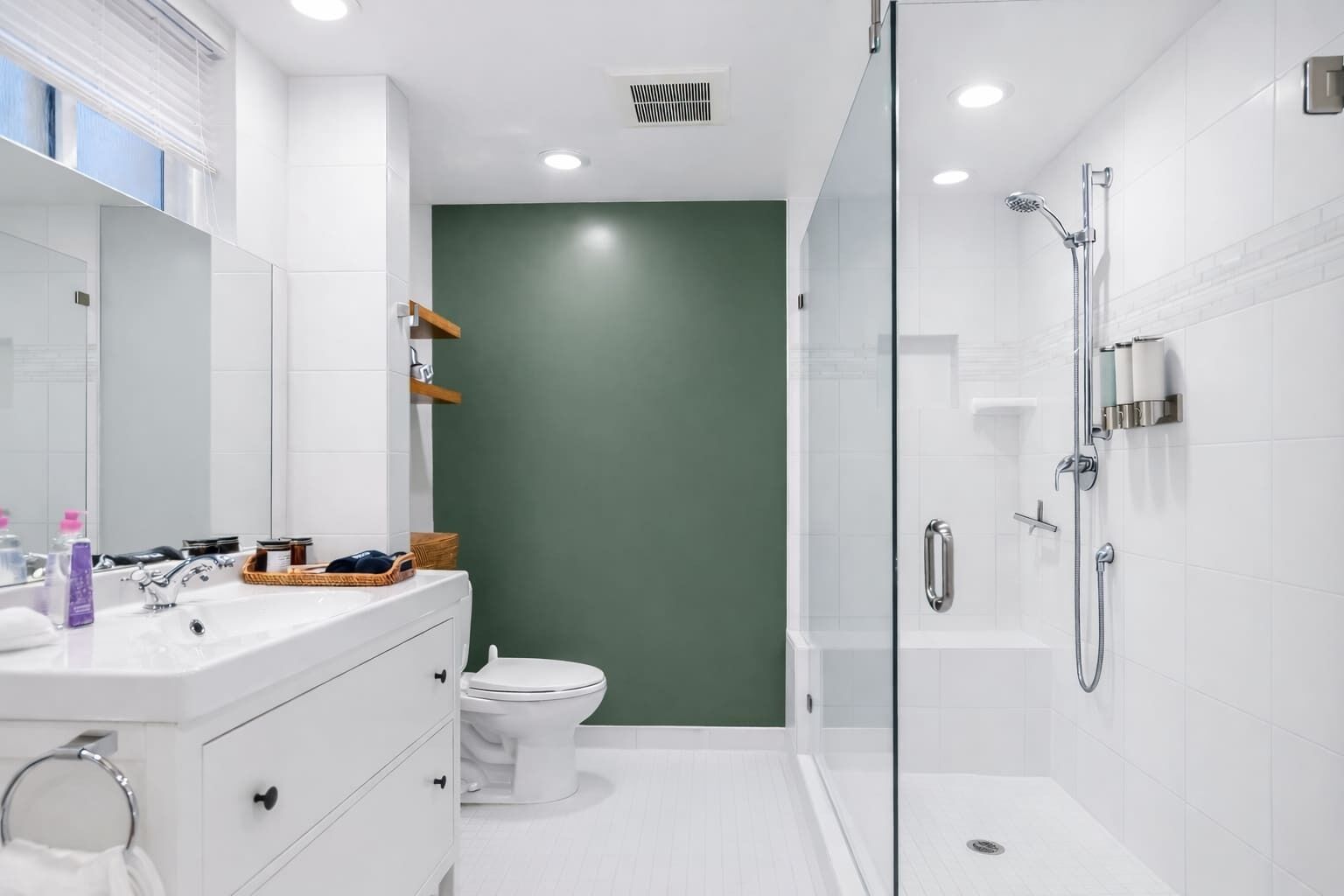 Een moderne badkamer met een douche met glazen wand, witte sanitair en een groene accentmuur.