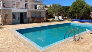 Ein Schwimmbecken mit einer Steindeckplatte, einem überdachten Sitzbereich und einem Gebäude mit Balkon.