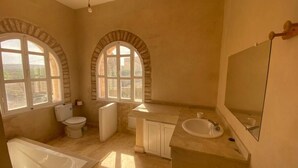 Ein Badezimmer mit Badewanne, Toilette, Waschbecken und bogenförmigen Fenstern.