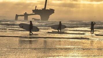 A beach scene with surfers and a large shipwreck in the background.