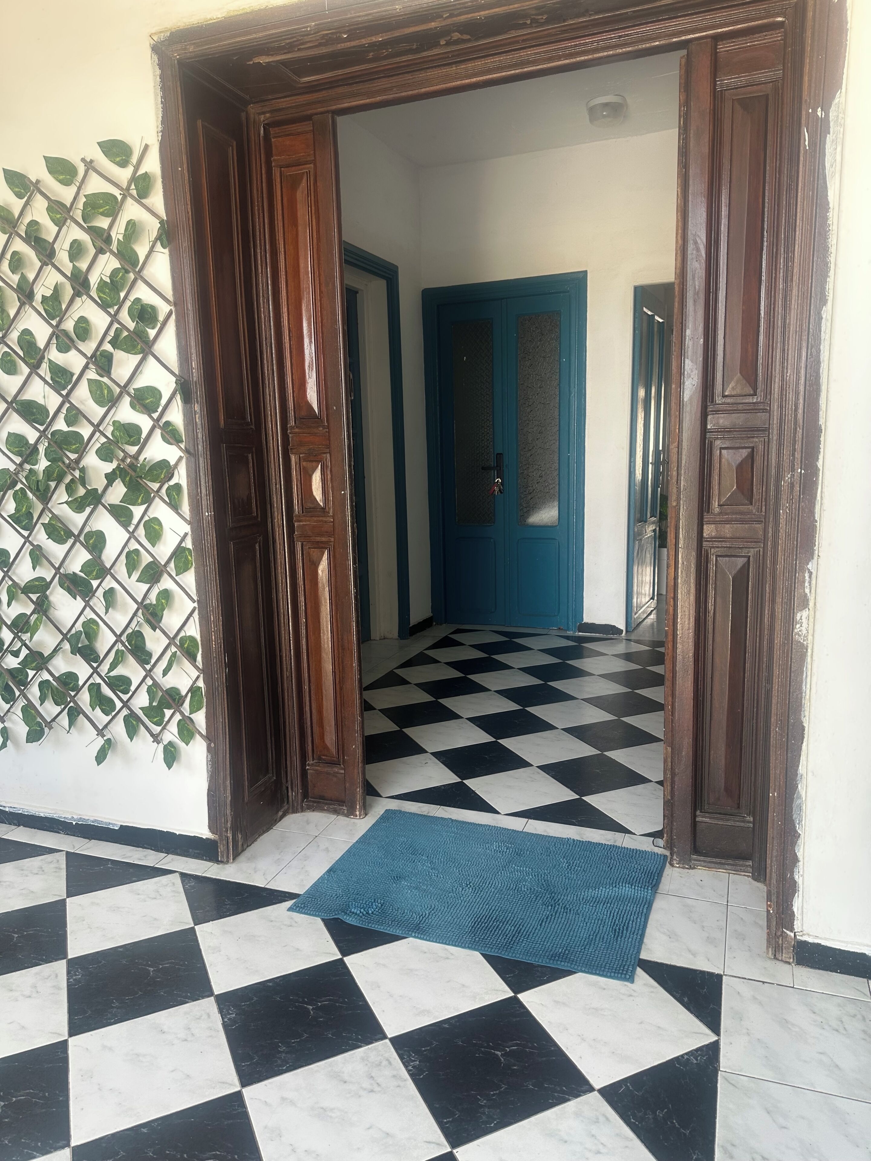 Um corredor com piso xadrez, porta azul e moldura de porta de madeira.