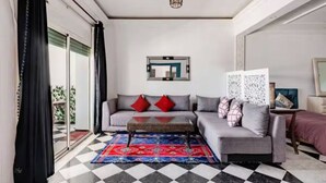 A living room with a checkered floor, a grey sofa with red and patterned cushions, a coffee table, and a large mirror on the wall. - Étage RDC Villa vu sur mer (El Jadida)