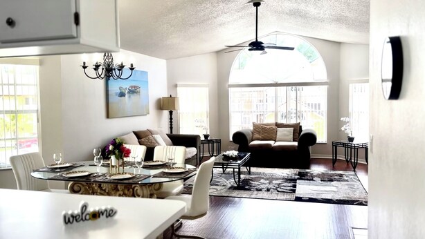 A spacious living room with a dining area, a ceiling fan, and large windows offering views of the city. - 	Resort-Style 3BR Condo (Kissimmee)