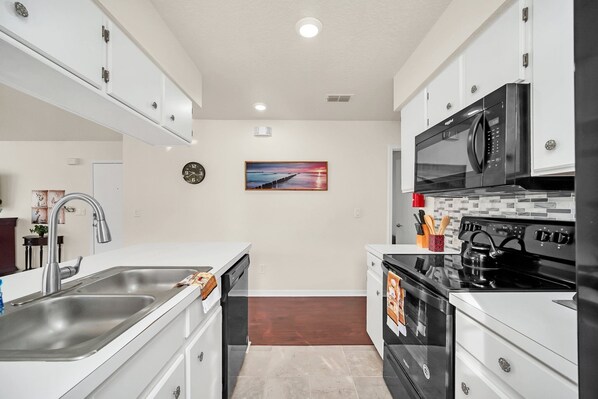 A modern kitchen with white cabinets, stainless steel appliances, and a wooden floor.