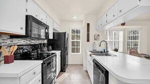 A modern kitchen with white cabinets, a black refrigerator, a microwave, and a kettle. - 	Resort-Style 3BR Condo (Kissimmee)