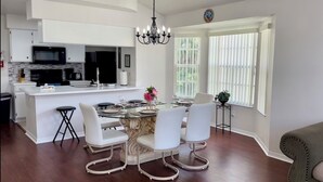 A modern kitchen with white cabinetry, a central island, and a dining area with a glass table and white chairs. - 	Resort-Style 3BR Condo (Kissimmee)