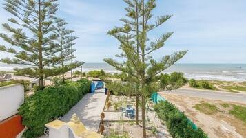 A coastal property with a paved pathway leading to a beach, surrounded by greenery and a clear view of the ocean.