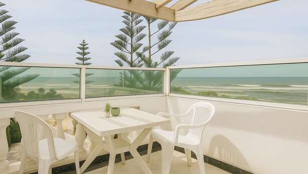 Ein Balkon mit Tisch und Stühlen mit Blick auf einen Strand und Palmen.
