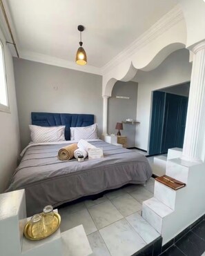 Ein ordentlich eingerichtetes Hotelzimmer mit Bett, Nachttisch, Lampe und Blick ins Freie.