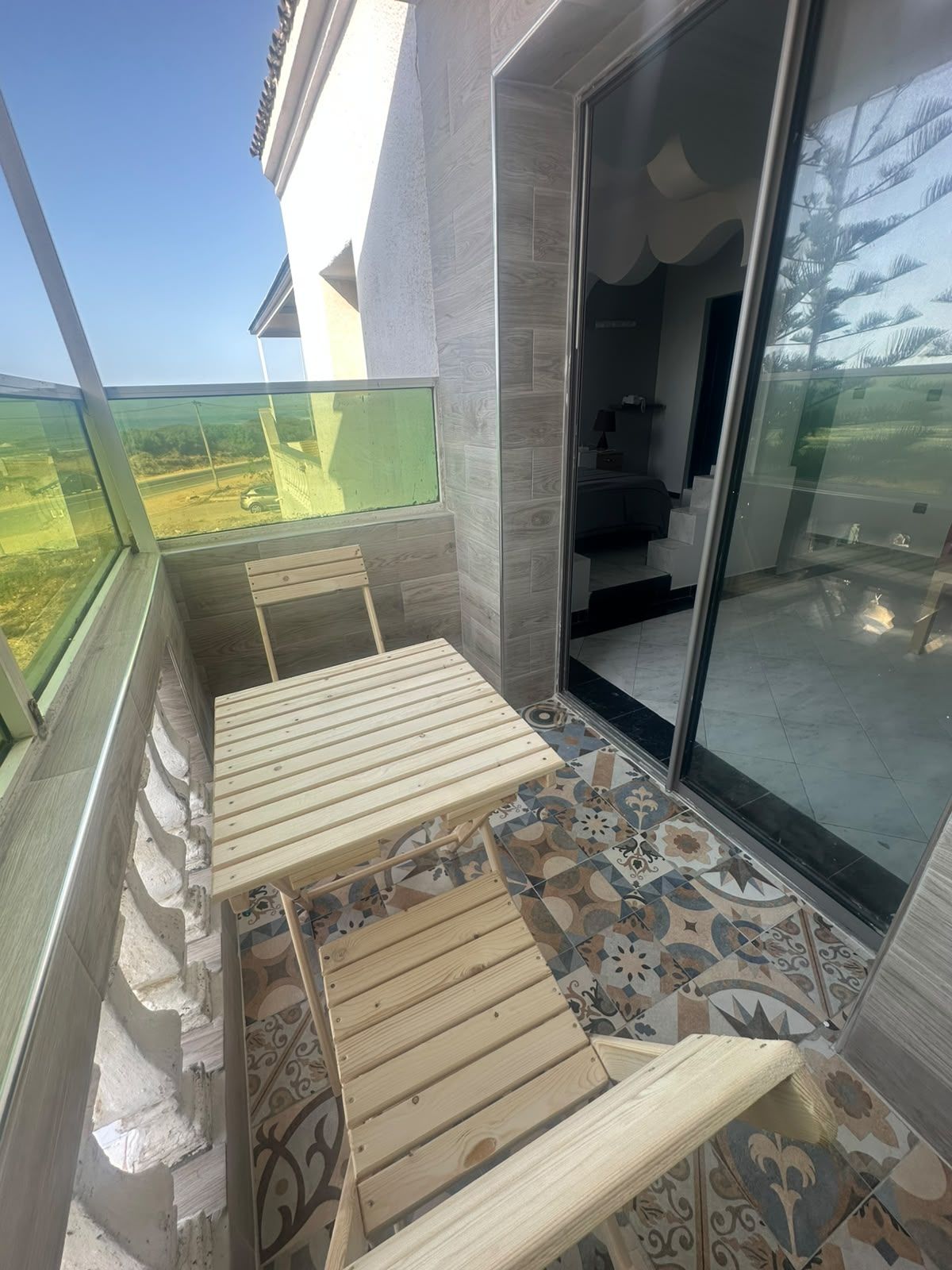 Ein Balkon mit Holztisch und -stühlen, einem gemusterten Boden und Blick auf die Landschaft.
