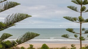 Blick auf einen Sandstrand, das Meer und etwas Grün.
