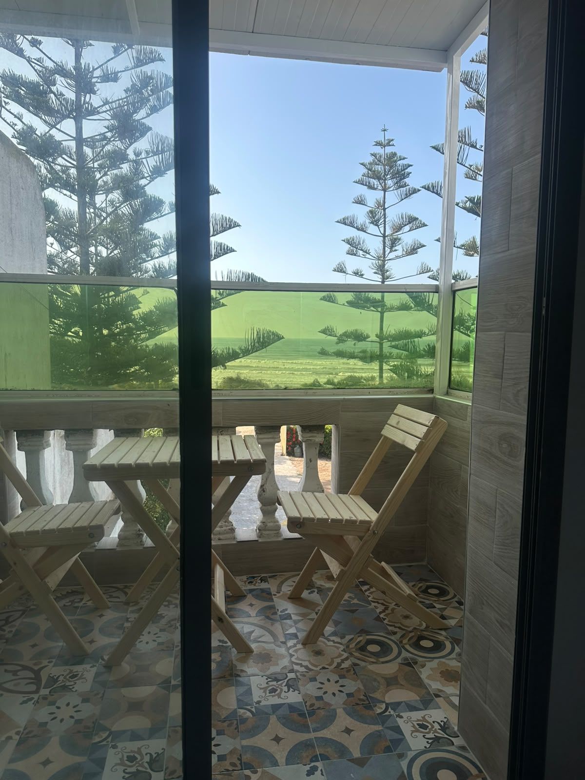 A room with a view of a green landscape, a wooden table, and patterned floor tiles.