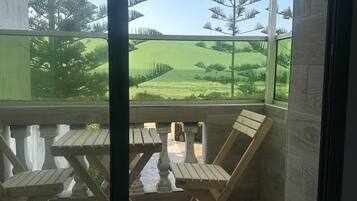 A room with a view of a green landscape, a wooden table, and patterned floor tiles.