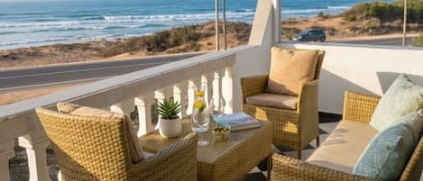 Een balkon met rieten meubels, een geruite vloer en uitzicht op de oceaan.