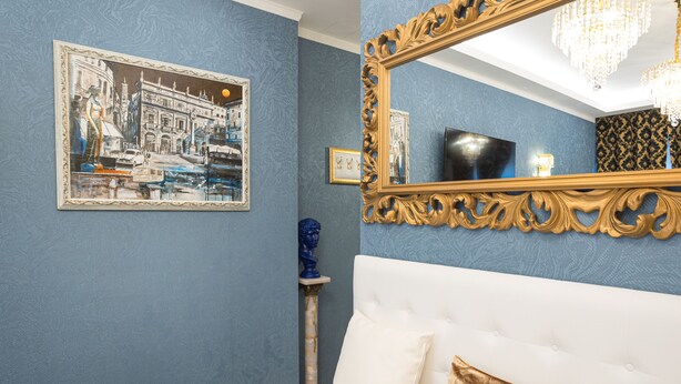 Un dormitorio con una cama blanca, un espejo grande y decorado, y un cuadro de un paisaje urbano enmarcado en la pared.