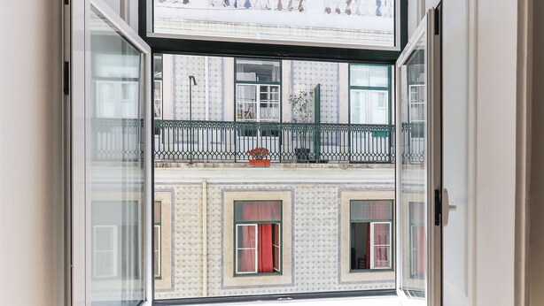 Vista da un balcone con parete esterna decorata, ringhiera in metallo e una pianta in vaso.