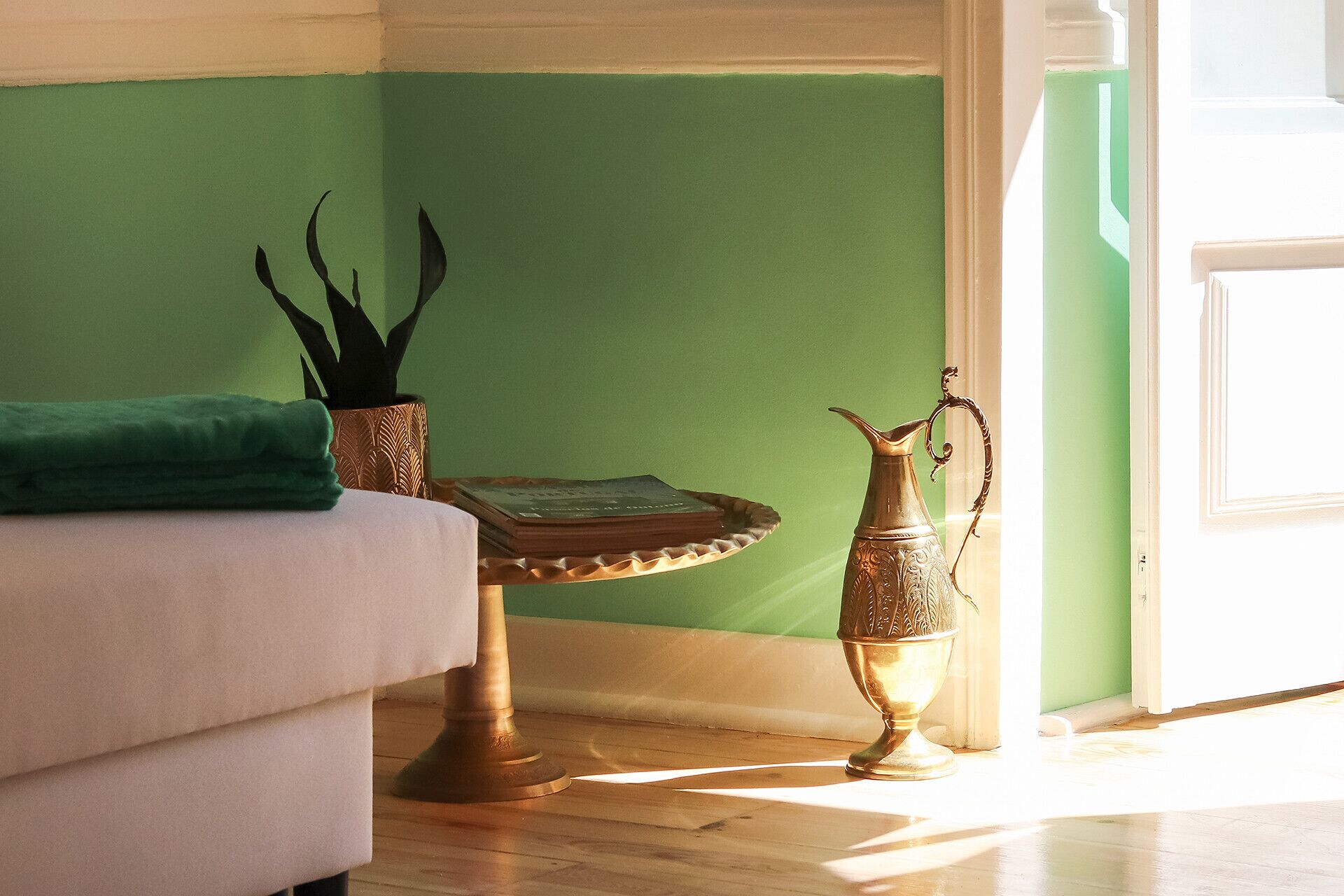 Una habitación con pared verde, sofá blanco, una mesita con bandeja y dos jarrones metálicos decorativos.