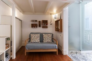 A cozy room with a wooden bed, a small shelf with decorative items, and a glass door leading to a balcony. - Santos Tiny Studio by Homing (Lisbon)