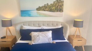 A bedroom with a large bed, two bedside tables, and a painting of a beach scene.