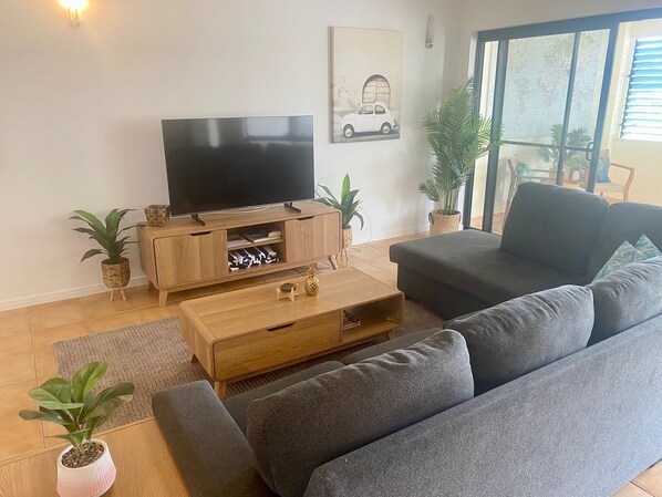 Una sala de estar moderna con un televisor de pantalla plana sobre un soporte de madera, un sofá gris y dos plantas en macetas.