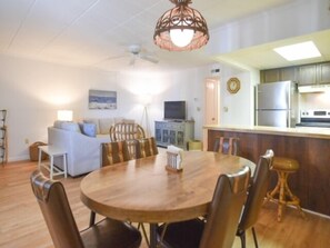 Un comedor con una mesa redonda de madera y sillas, un ventilador de techo y una cocina al fondo.