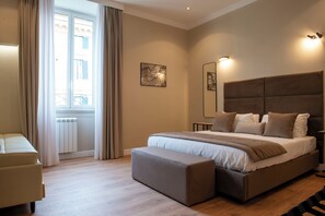 A modern bedroom with a large bed, a bench, a chair, and a view of the street through a window. - HOTEL AD Suites Nazionale (Rome)