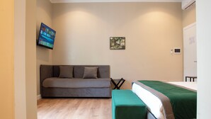 A bedroom with a sofa bed, a single bed with a green bedspread, a wall-mounted TV, and a small artwork. - HOTEL AD Suites Nazionale (Rome)