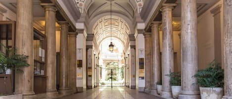 A corridor with large columns, a tiled floor, and a central light fixture.