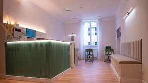 A hotel reception area with a green reception desk, a seating area with a bench, and a window with blinds. - HOTEL AD Suites Nazionale (Rome)