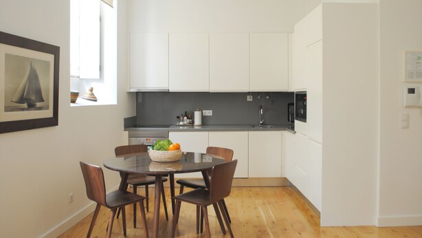 Una cocina moderna con armarios blancos, encimera negra y un comedor con una mesa redonda y cuatro sillas.
