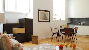 Una sala de estar moderna con un sofá, una mesa de comedor con sillas, una zona de cocina y un cuadro en la pared.