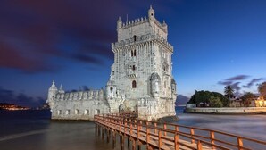 Un château de pierre historique, doté d’une tour imposante, d’une passerelle en bois menant à l’entrée et d’une étendue d’eau paisible au premier plan.