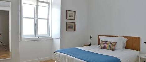 A bedroom with a bed, a window, and two framed pictures on the wall.