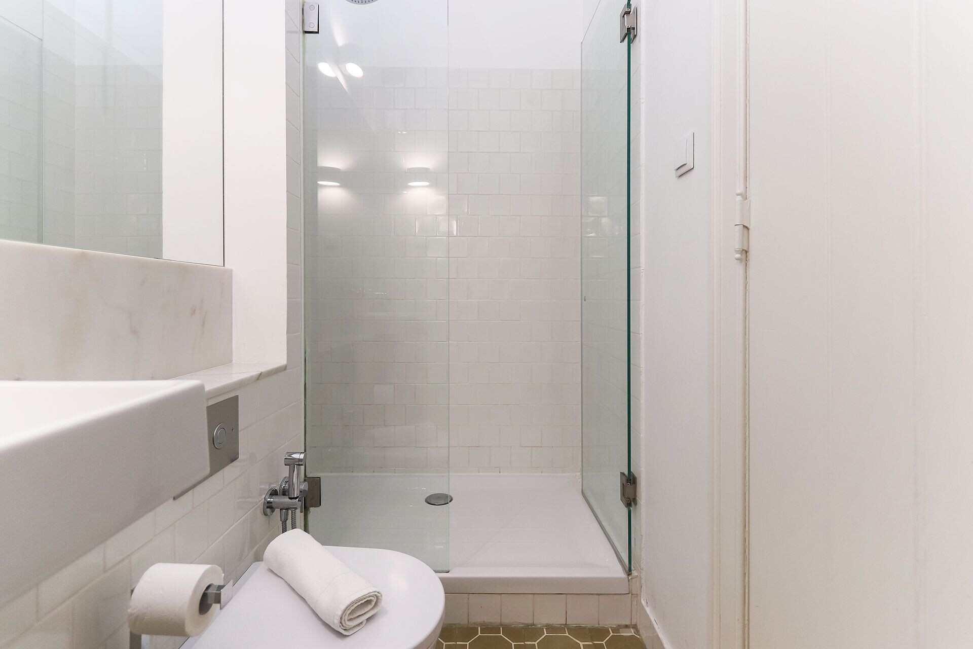 Un baño pequeño y blanco con ducha de vidrio, inodoro y lavamanos.