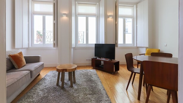 A living room with a sofa, a TV, a small table, and a dining area with chairs. - Alfama Deluxe by Homing (Lisbon)