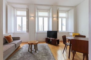 A living room with a sofa, a TV, a small table, and a dining area with chairs. - Alfama Deluxe by Homing (Lisbon)