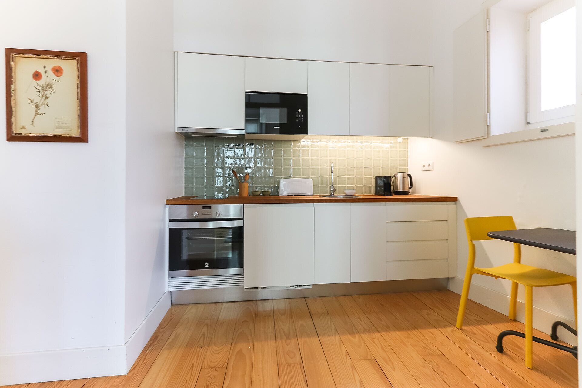 Una cocina compacta con gabinetes blancos, horno de acero inoxidable, microondas y encimera de madera.