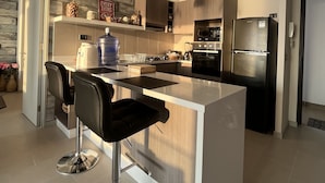Une cuisine moderne dotée d’un îlot central, de tabourets de bar, de luminaires suspendus et d’appareils électroménagers en acier inoxydable.