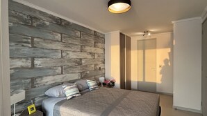 Une chambre moderne avec un grand lit, un mur d’accent en bois, une table de chevet avec une lampe et un tapis à motifs.