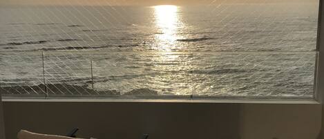 A balcony with a view of the ocean at sunset, featuring two chairs and a small table.